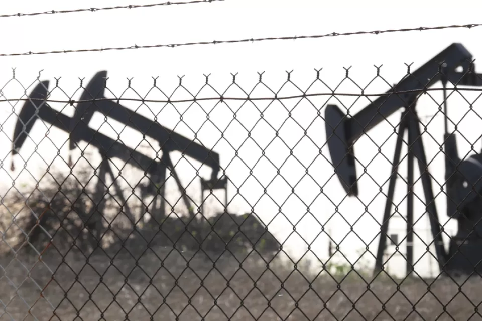 View of black oil wells behind chain link fence with barbed wire top